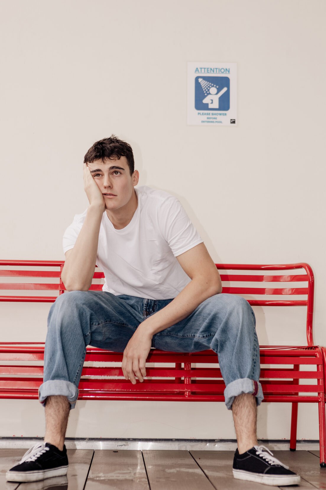 White man with brown hair sitting on a red, metal bench with his head in one of his hands looking defeated.