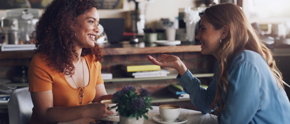 Two women sitting in a café and talking to each other, symbolizing "tips for making someone fall in love"