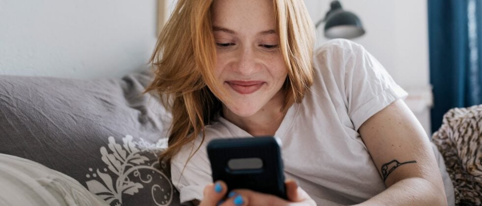 Woman lying in bed and smiling at her mobile phone as a symbol for online dating tips