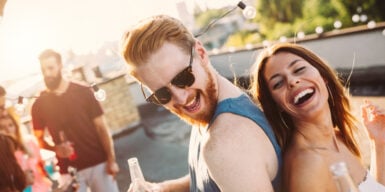 A man and a woman laughing and dancing back-to-back at a rooftop party.