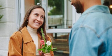 A woman smiling at a man with flowers in her hands.