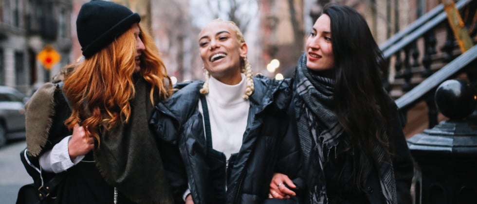 Three women walk together through the city arm in arm as a symbol of Polymory