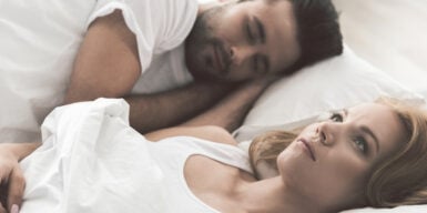 Couple in bed with the man sleeping and woman lying there thinking