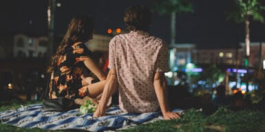 A young couple sitting on a picnic blanket in the park at night