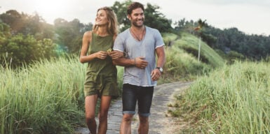 Couple walking along a scenic path while holding hands & smiling