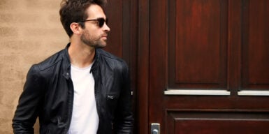 A guy in a leather jacket and sunglasses looking away as he walks